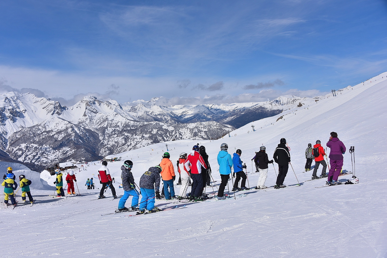 A large group of skiers who have stopped on the mountain, all in different coloured ski jackets.