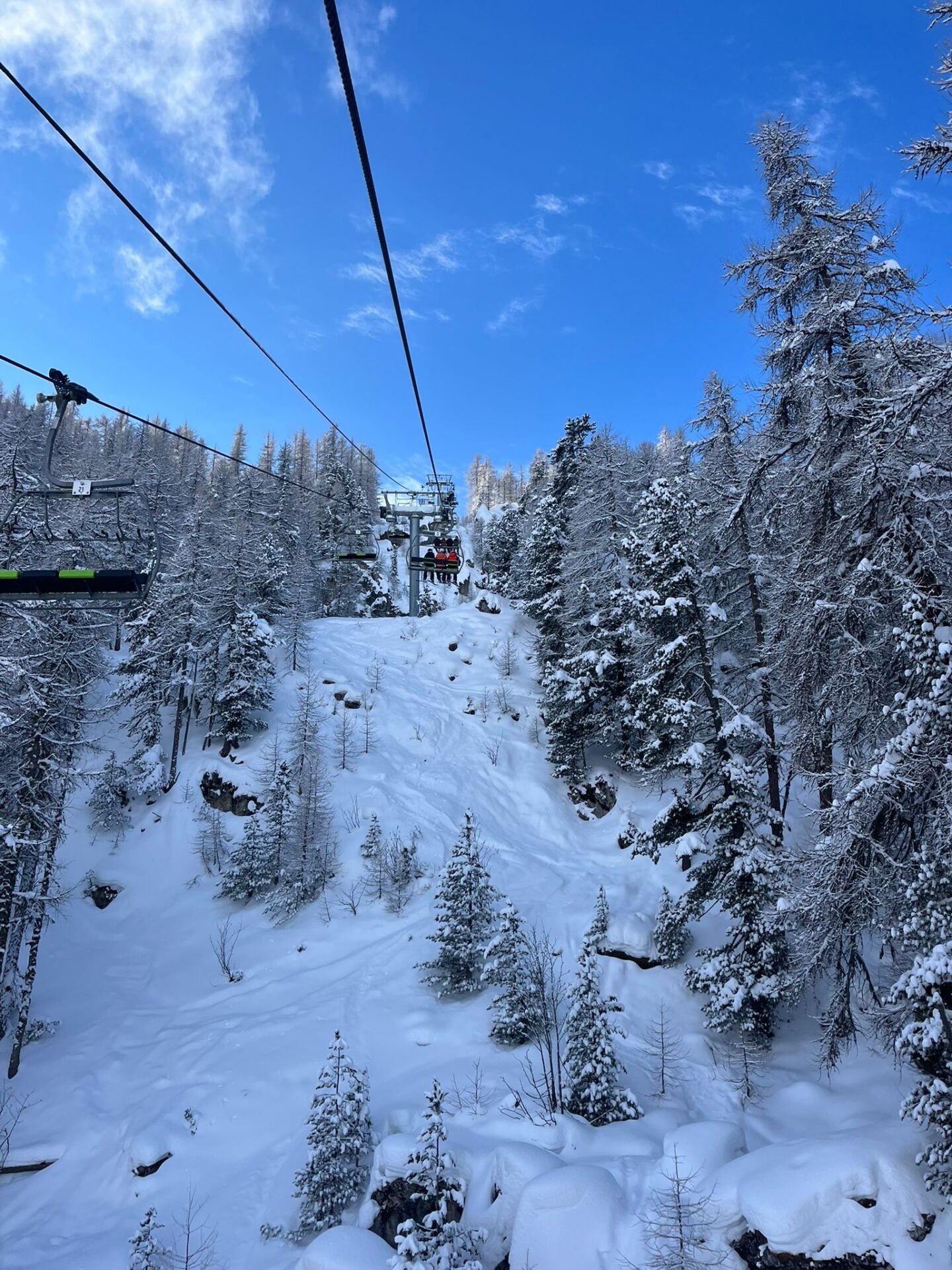 On a chairlift in Serre Chevalier, the lift is tree lined and there is plenty of snow.