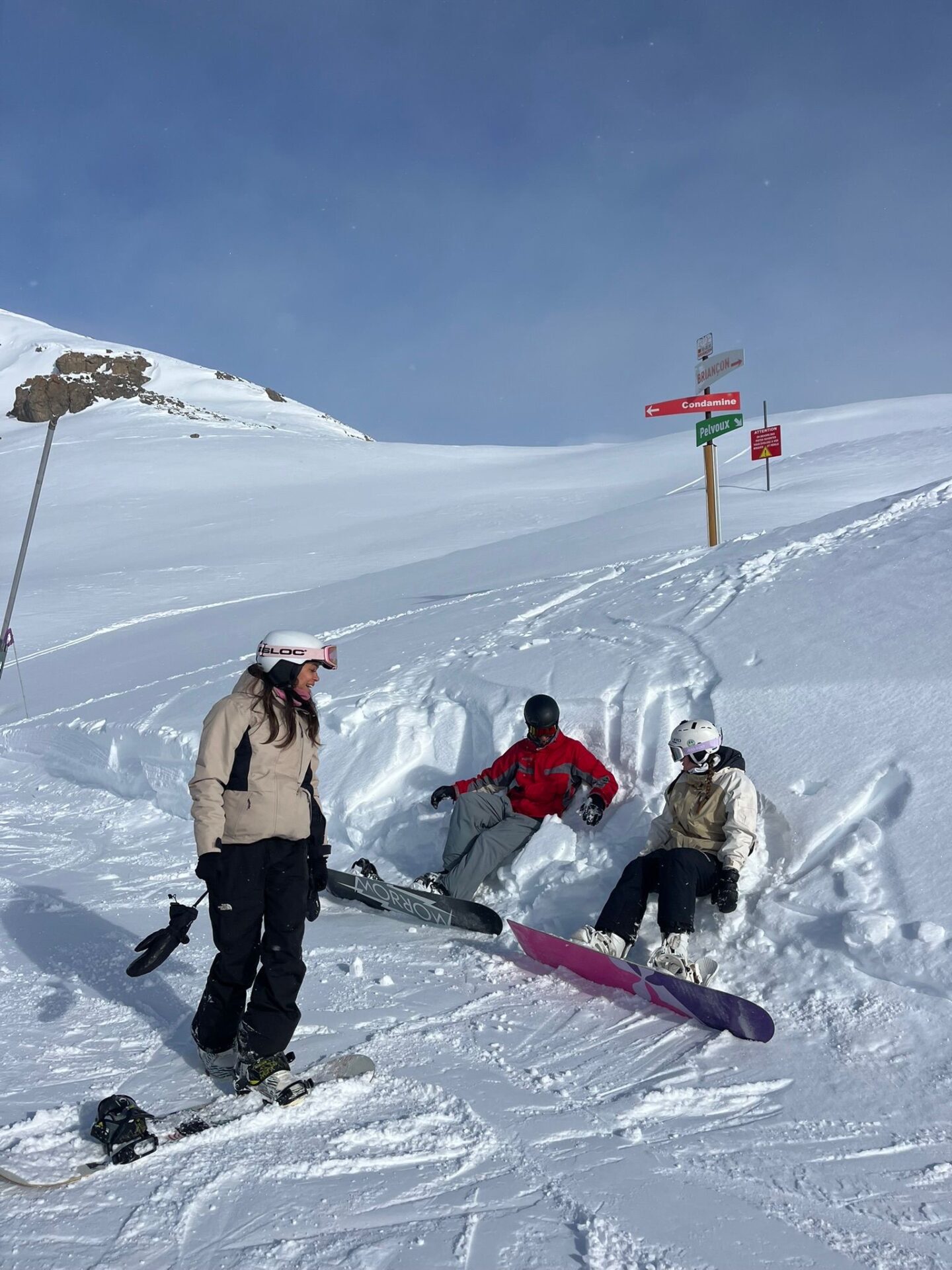 Three snowboarding at the side of the piste, two of which are sitting down.