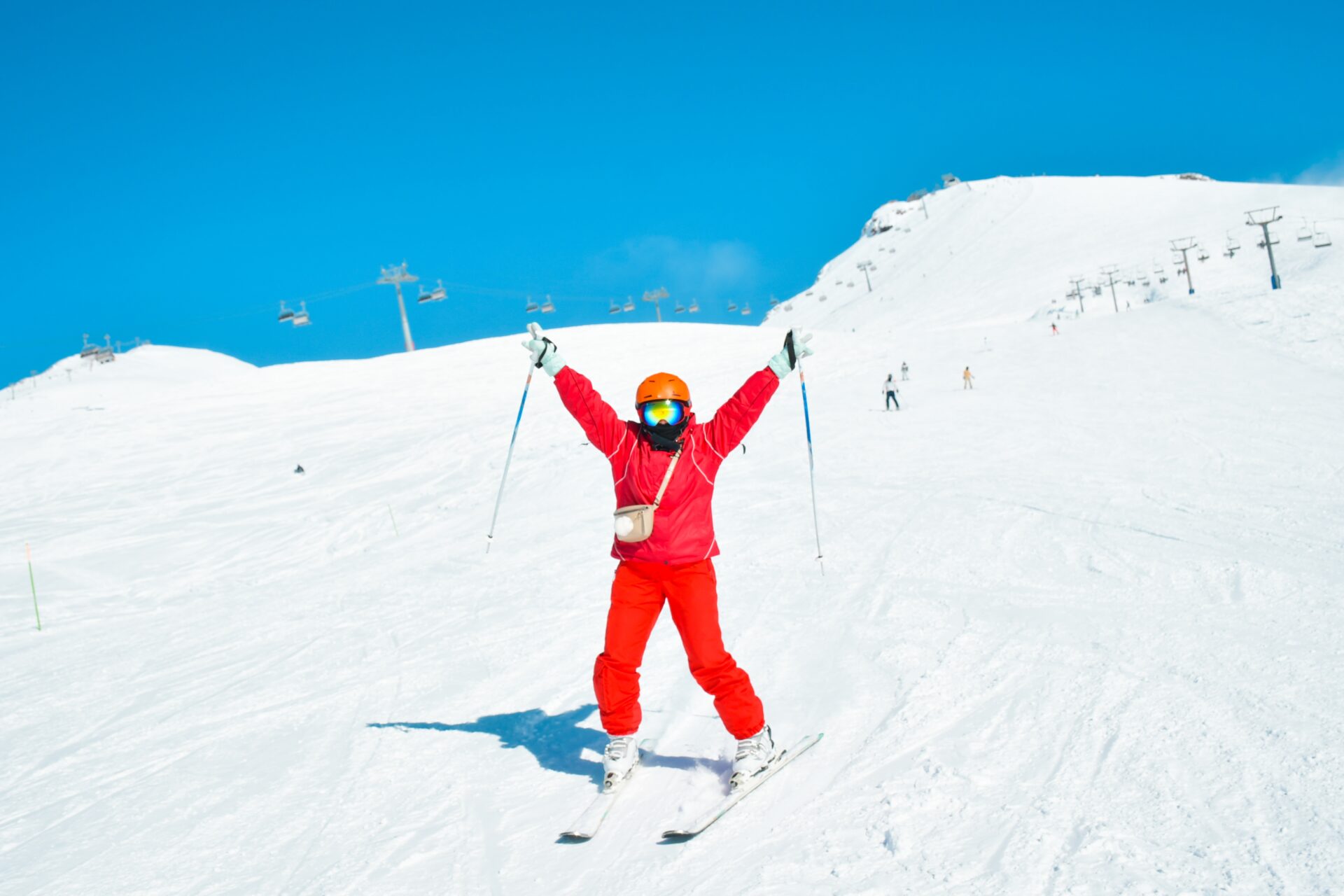A skiier in a red all in one skiing down the mountain with their hands in the air.