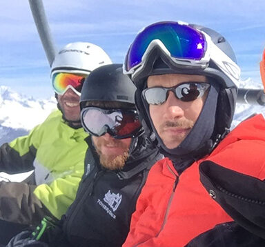 Four skiers on a chairlift, they are wearing bright coloured ski googles and ski jackets
